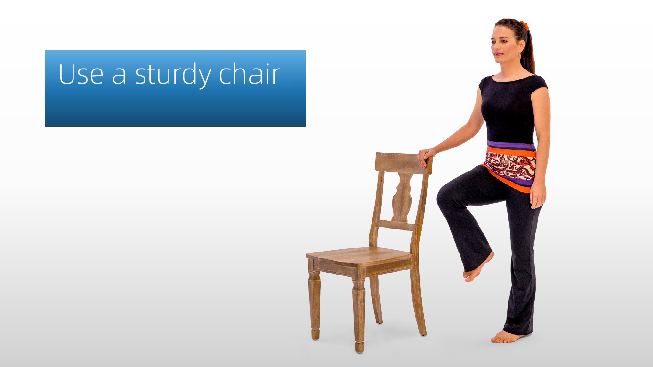 Woman seated on a sturdy wooden chair with a 'Use a sturdy chair' label, demonstrating proper chair selection for yoga